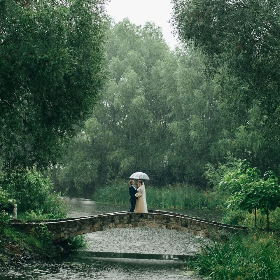 A couple under one umbrella, crossing a stone bridge in the rain