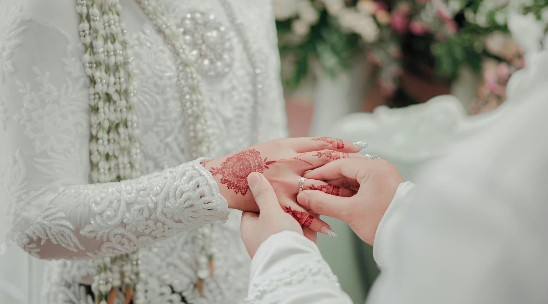 Hands decorated with henna as a ring is placed at a wedding ceremony